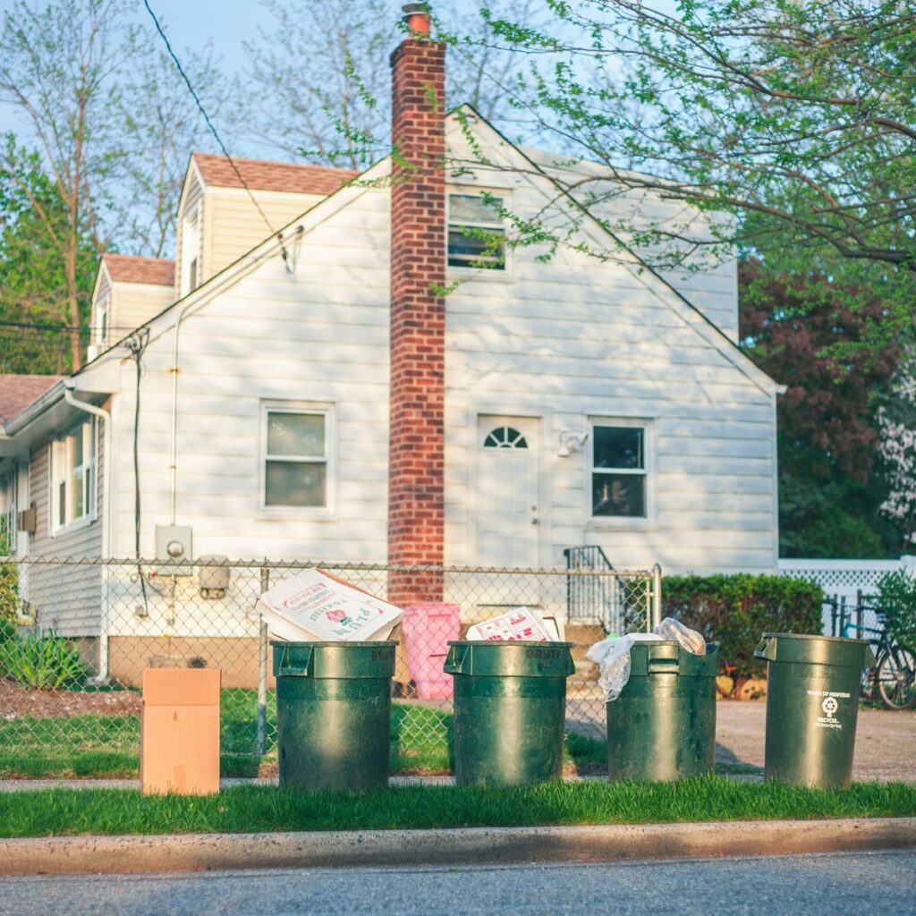 Residential home with multiple curbside trash bins and discarded household items, representing efficient dumpster rental in Hart, MI.