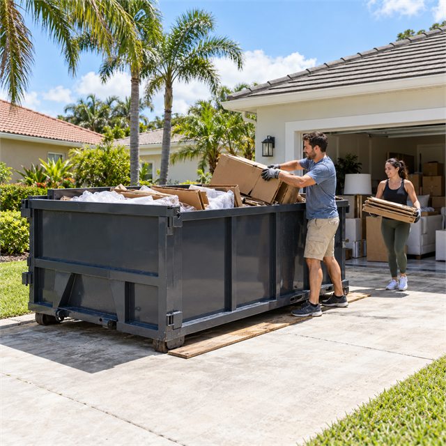 Homeowners loading cardboard boxes and household clutter into a roll-off dumpster during dumpster rental services in Ada, MI